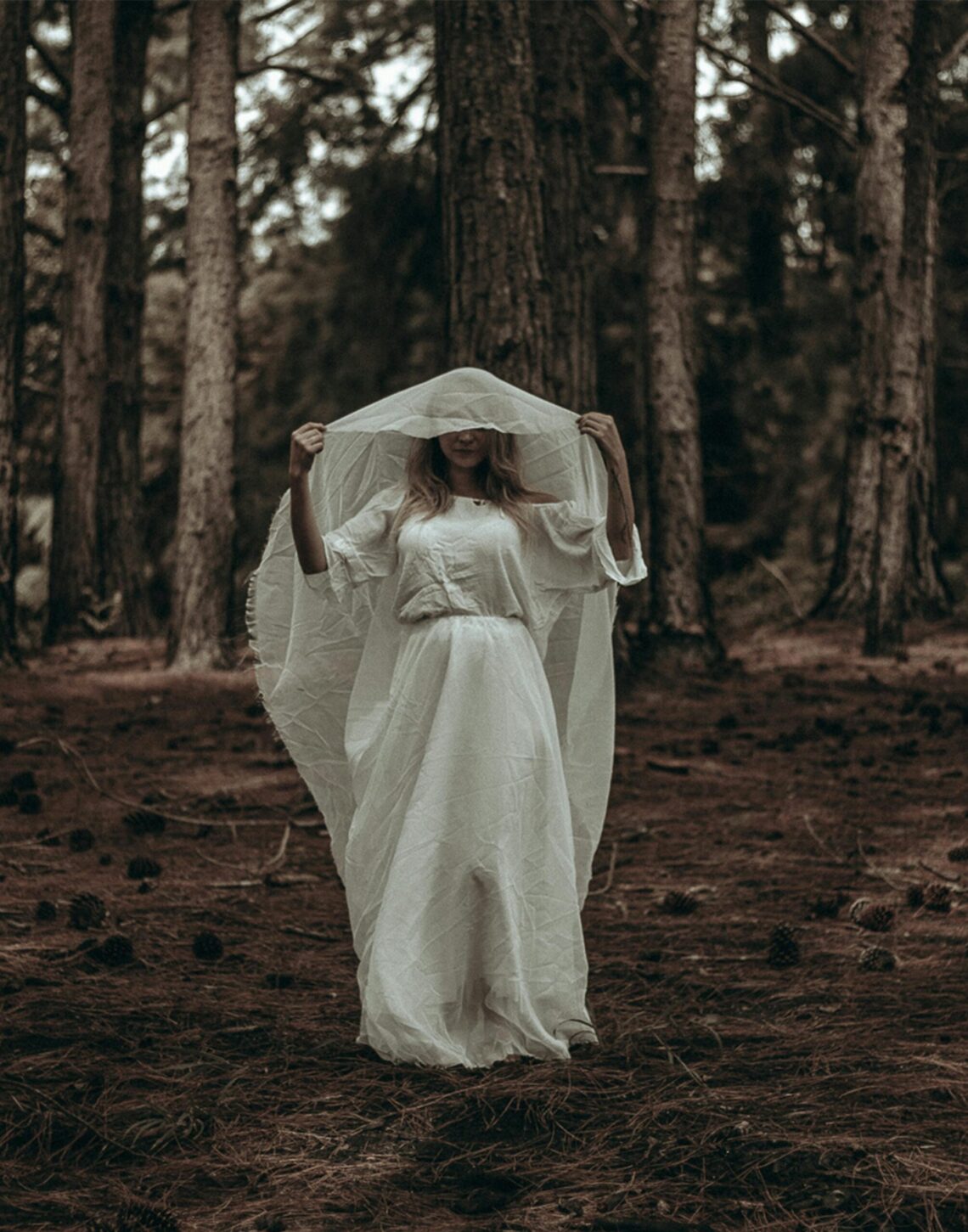 A woman in a white dress stands in a dark, eerie forest creating a mysterious atmosphere.